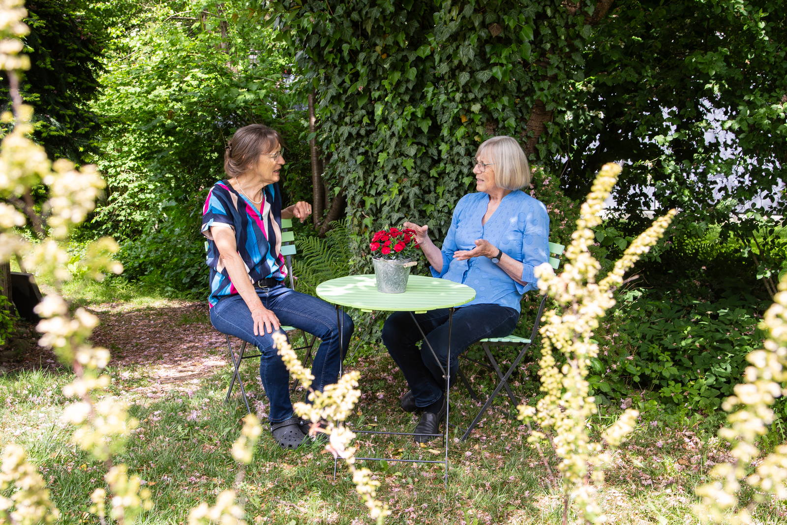 Zwei Frauen im Gespräch an einem grünen Gartentisch im Garten von d'Herberg